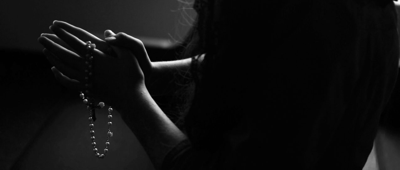 silhouette of woman holding rosary while praying